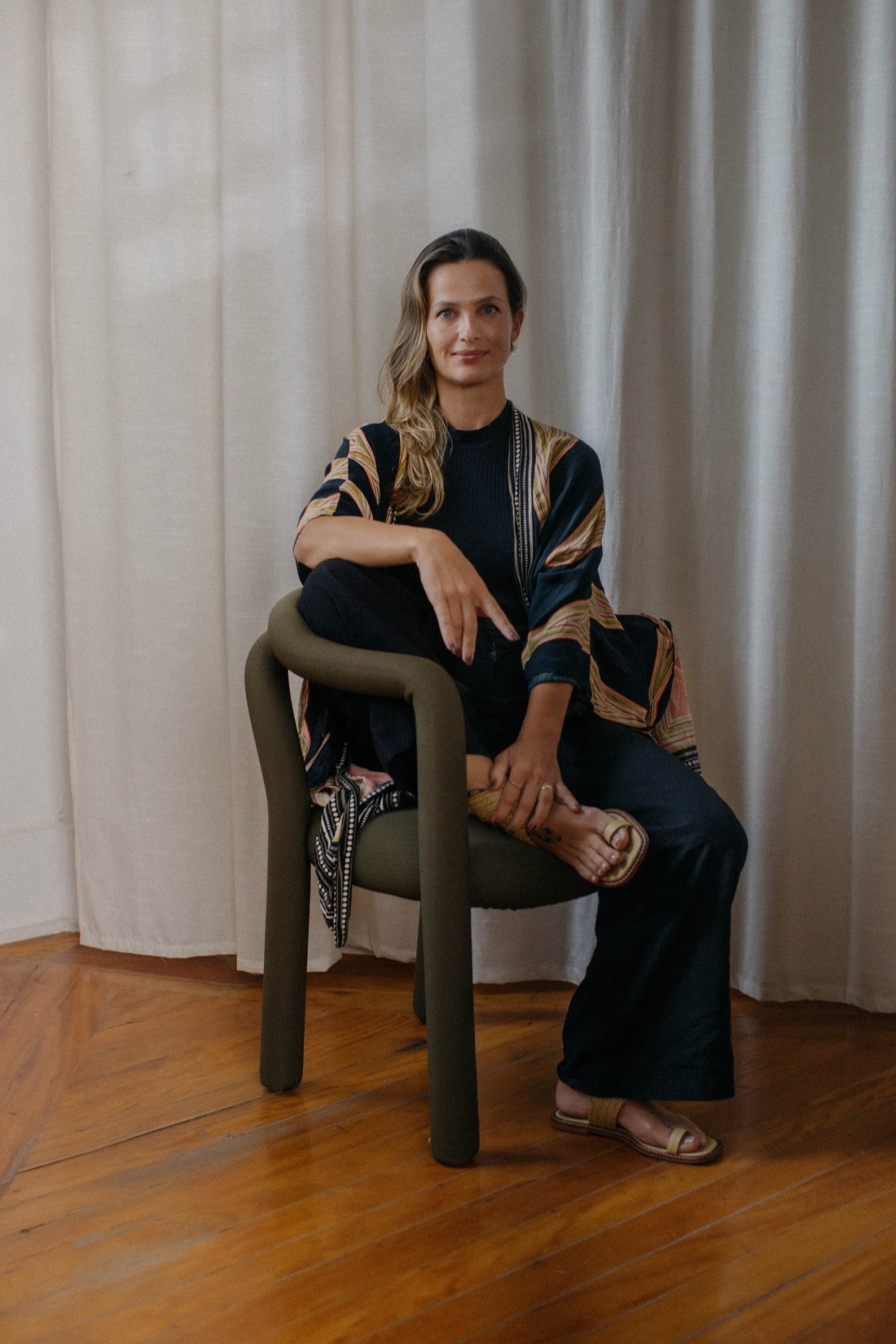 Manuela Vitiello sentada em uma cadeira verde, em frente a uma cortina clara